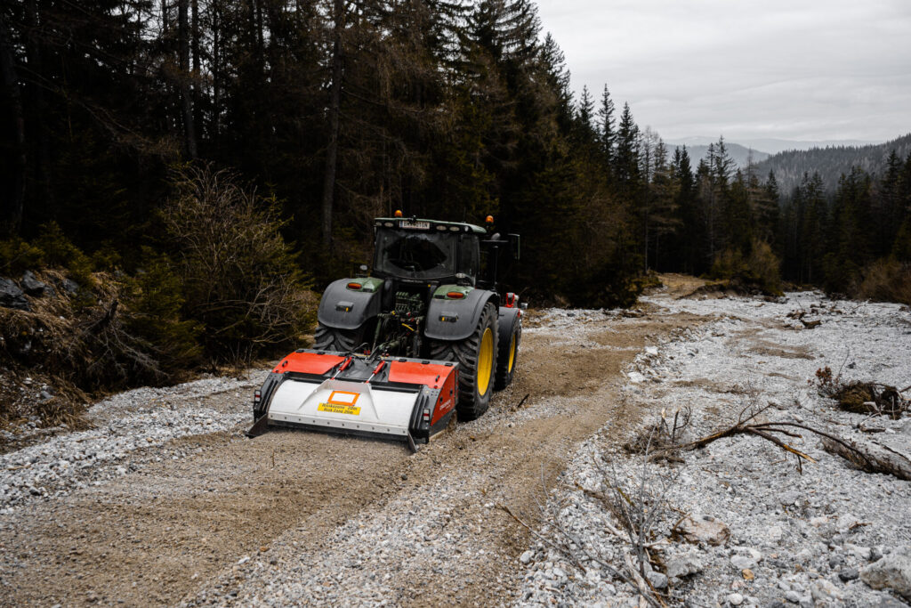 raktor mit Wegefräse bei der Sanierung eines Forstwegs in alpinem Gelände. Das Bild zeigt den professionellen Wegebau durch Erdbau Bayer in der Steiermark.